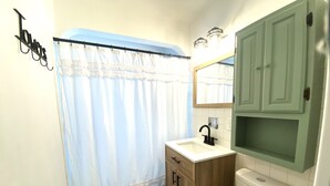 A bathroom with a shower curtain, a sink, a toilet, and wooden cabinets. - Pekin Cottage (Pekin)