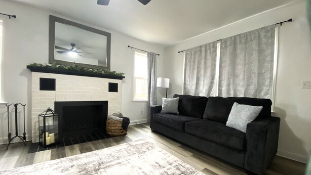 A living room with a fireplace, a black sofa, a patterned rug, and a ceiling fan. - Pekin Cottage (Pekin)