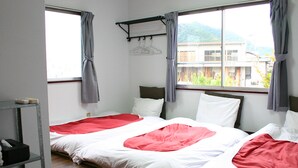 A room with two beds, a window with a view of buildings and greenery, a shelf with items, and a wall-mounted rack with hangers. - RETRO (Fujikawaguchiko)