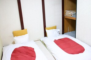 Two single beds with red and white bedding, a yellow pillow, and a wooden shelf with folded towels. - RETRO (Fujikawaguchiko)