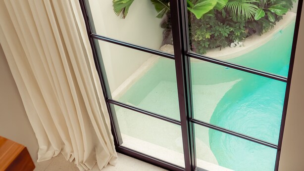 A wooden staircase leading to a balcony with a view of a pool and tropical plants. - Vesna Townhouse 1 (Canggu)