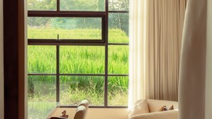 A modern room with a large window, a curved sofa, a dining table with chairs, and a ceiling fan. - Vesna Townhouse 1 (Canggu)