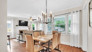 Un coin repas avec une table et des chaises en bois, un lustre et un téléviseur en arrière-plan.