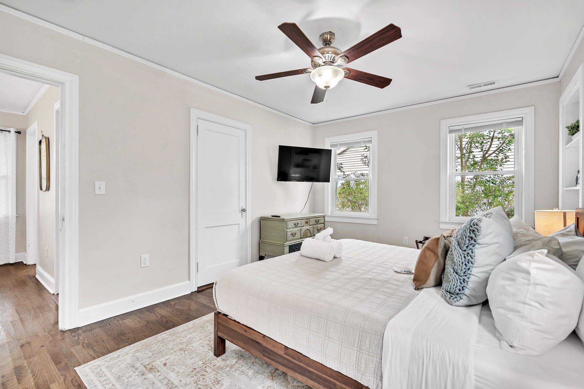 A bedroom with a bed, a ceiling fan, a TV, and a window.
