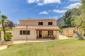 Una casa de dos plantas con techo de tejas, un porche cubierto con mobiliario exterior y un césped bien cuidado.