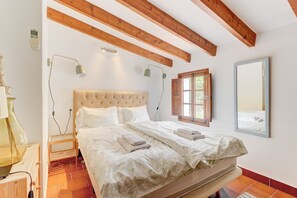 Un dormitorio con una cama grande, vigas de madera, un ventanal y un espejo.