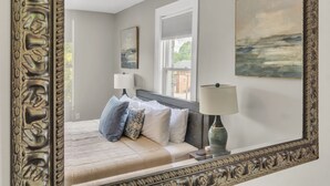 Um quarto com uma cama grande, duas luminárias de cabeceira, uma janela com persianas e um quadro na parede.
