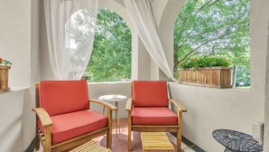 Uma varanda acolhedora com duas cadeiras vermelhas estofadas, uma mesa redonda pequena e um banco de madeira.