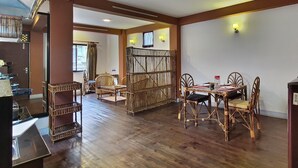 Habitación de hotel con suelo de madera, mobiliario de mimbre, una mesa de comedor con sillas, un dispensador de agua y una tetera sobre un mueble.