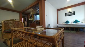 Una habitación con una mesa de vidrio, muebles de mimbre, una cama con almohadas y un cuadro colgado en la pared.