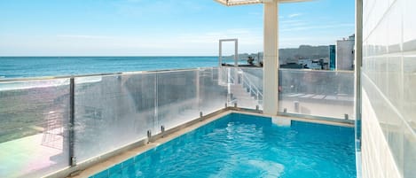 Un espace piscine offrant une vue sur l’océan, une terrasse couverte et une balustrade en verre.