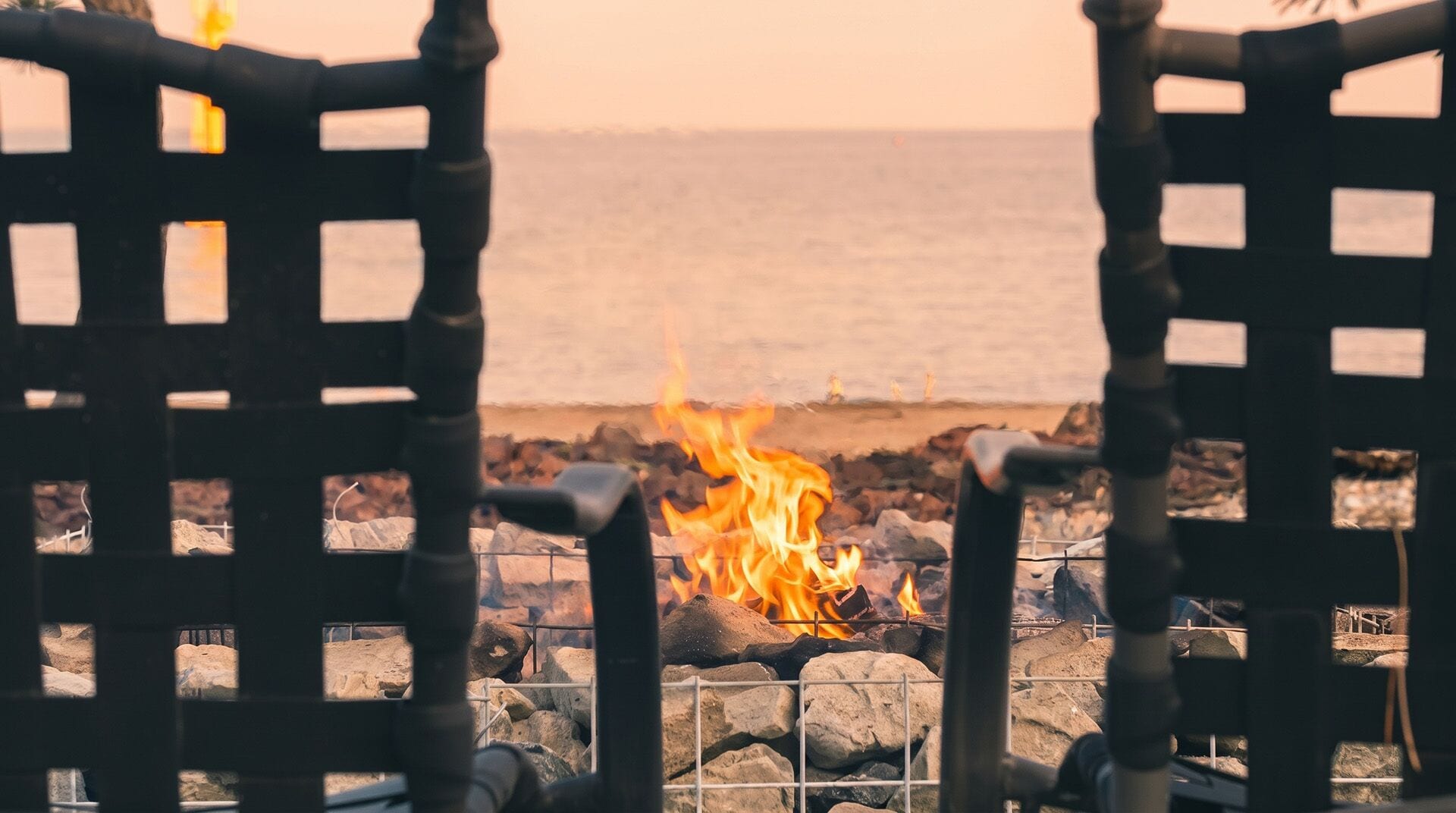 Two chairs facing a fire with a view of the ocean.