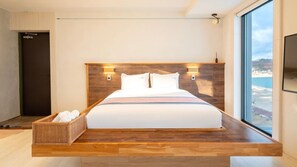 Habitación de hotel moderna con una cama grande, cabecero de madera y vista al mar.