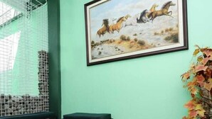 Ein Zimmer mit grüner Wand, einem gerahmten Gemälde von Pferden, einem Holztisch, einer kleinen Bank und einem Blumentopf.