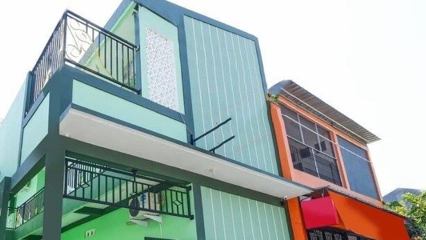 Ein mehrstöckiges Haus mit einer Fassade in Grün und Orange, einem Balkon und einem verschlossenen Eingang.