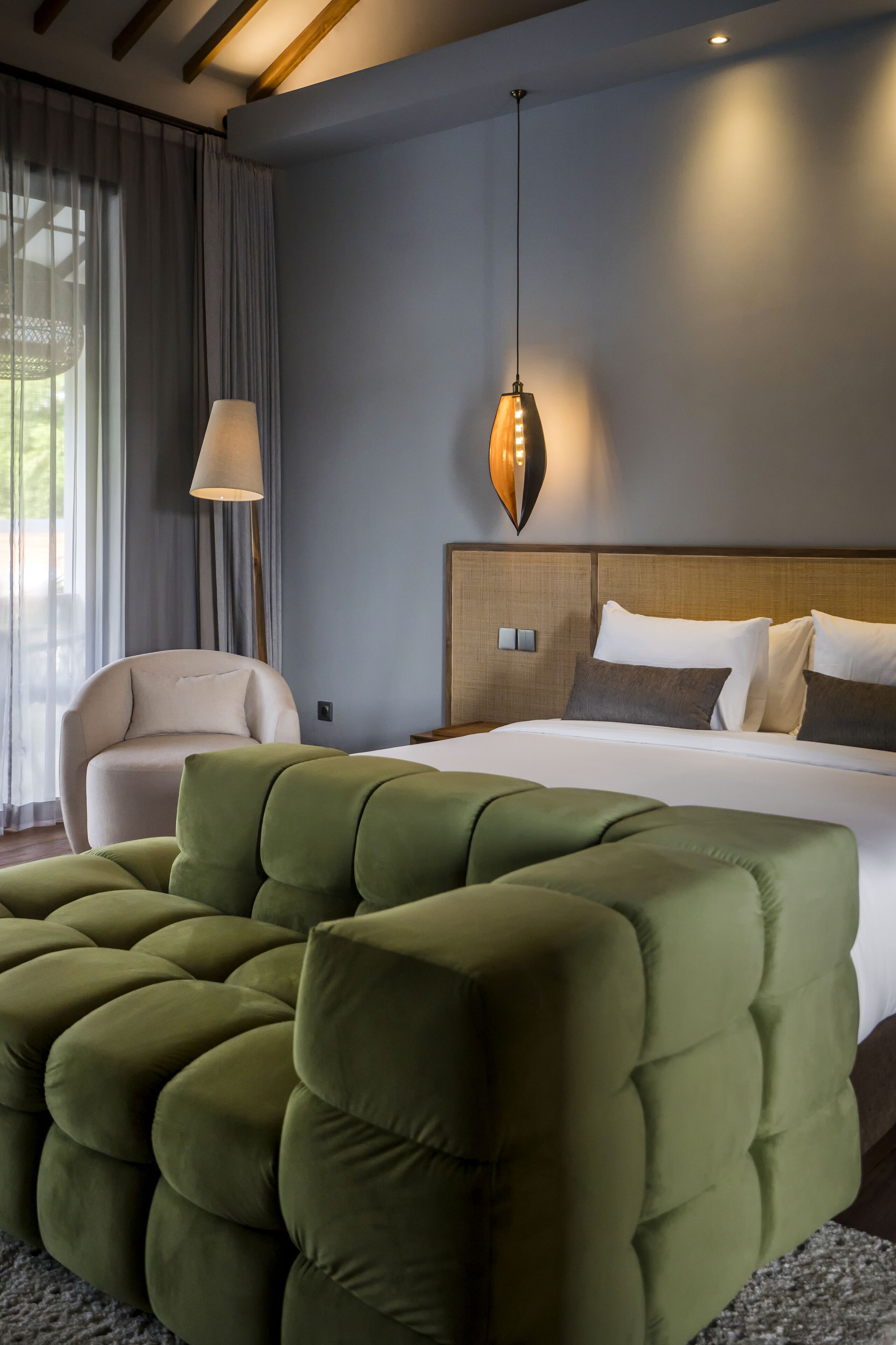 Ein modernes Hotelzimmer mit einem großen Bett, einer grünen Sitzbank, einem Sessel und einer hängenden Pendelleuchte.