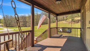 A wooden deck with a swing, a view of a grassy area, and an American flag. - Pet-Friendly Cabin in Marietta w/ Porch Swings (Cleveland)