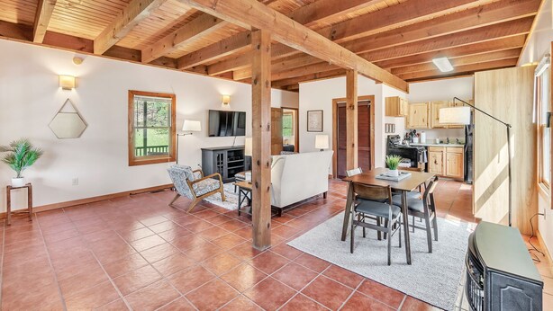 A spacious living area with a high wooden ceiling, a dining table, and a kitchen in the background. - Pet-Friendly Cabin in Marietta w/ Porch Swings (Cleveland)