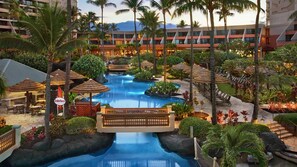A resort with a central pool, palm trees, and a bridge.