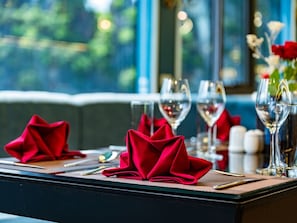 A table set with red napkins, wine glasses, and cutlery, with a window view in the background. - Maia Cruise (Tuan Chau)