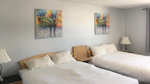 Una habitación de hotel con dos camas, una mesita de noche con lámpara y dos cuadros en la pared.