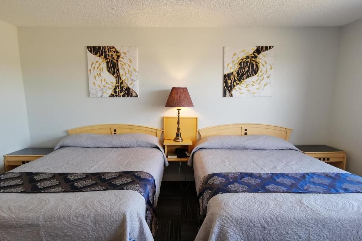 Une chambre double avec deux lits, une table de chevet, une lampe et deux œuvres d’art murales.