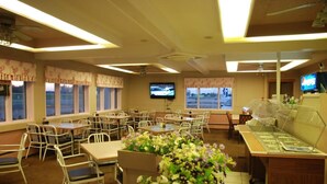 Un restaurante con varias mesas y sillas, una zona de bufé y una pantalla de televisión.