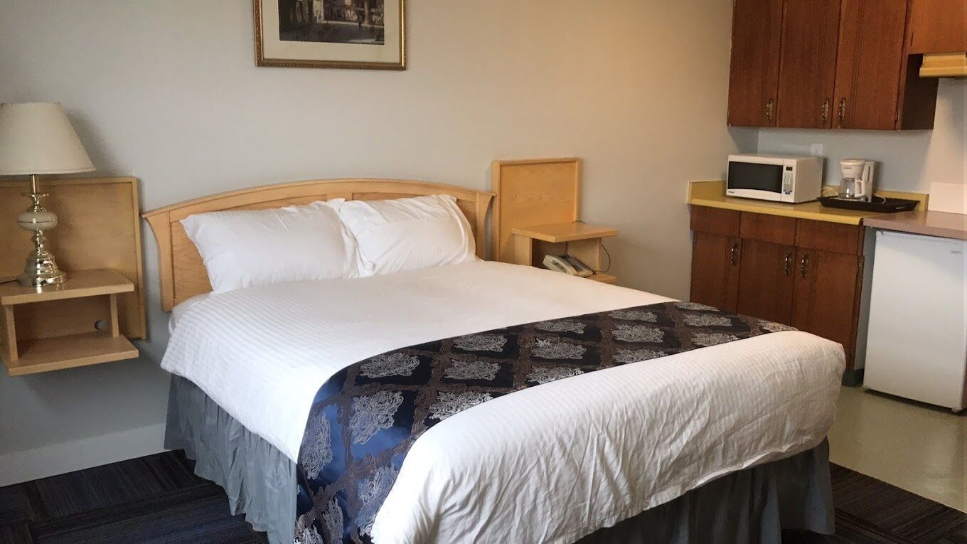 A hotel room with a bed, a nightstand, a lamp, a microwave, and a small kitchenette.