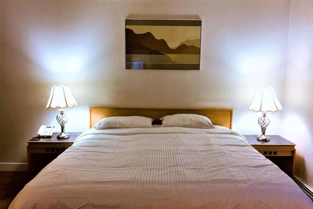 Une chambre d’hôtel avec un grand lit, deux tables de chevet avec des lampes, un tableau au mur et un téléphone sur l’une des tables.