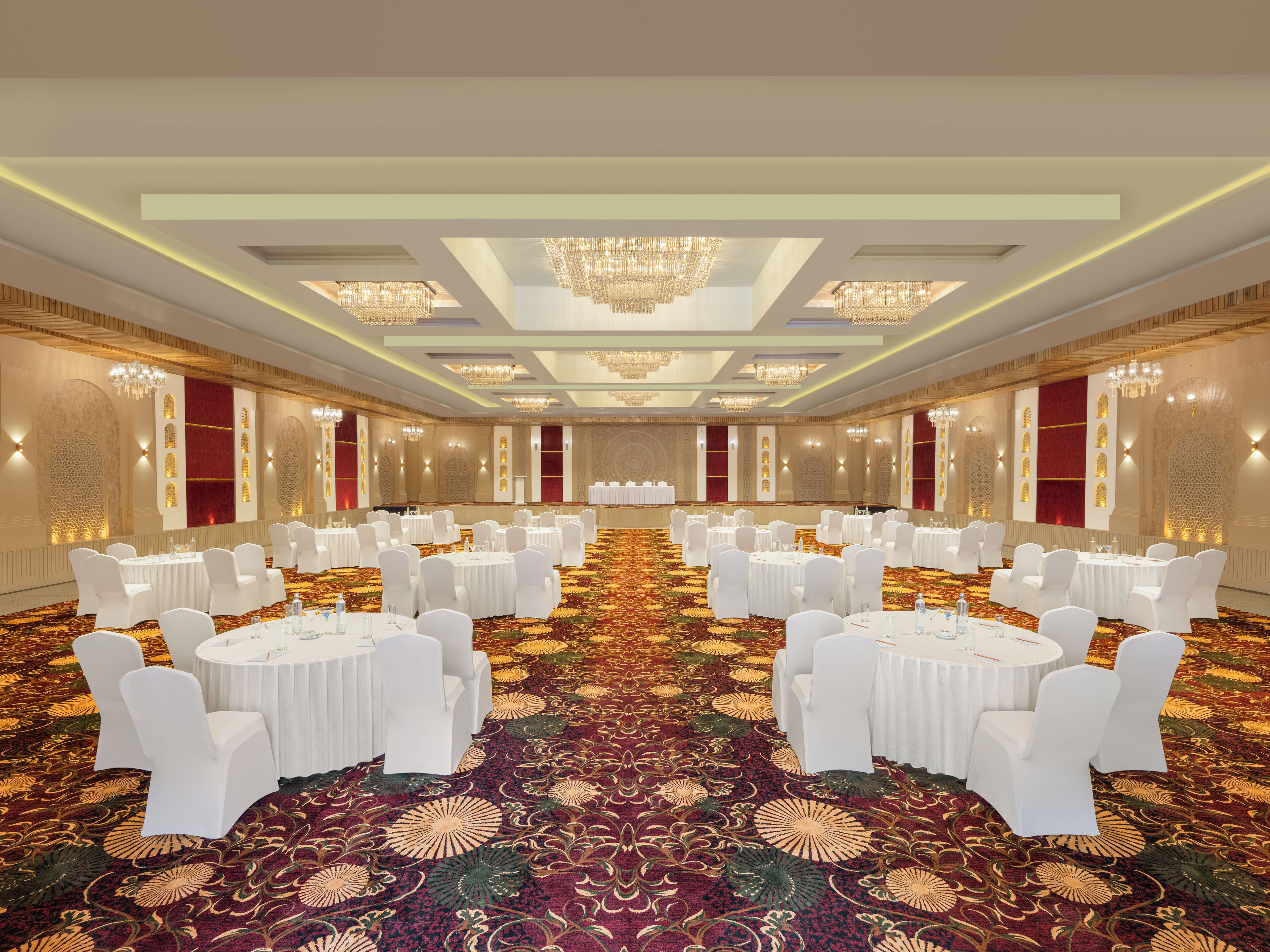 Une grande salle de conférence avec des tables rondes et des chaises blanches, une moquette à motifs et des lustres.