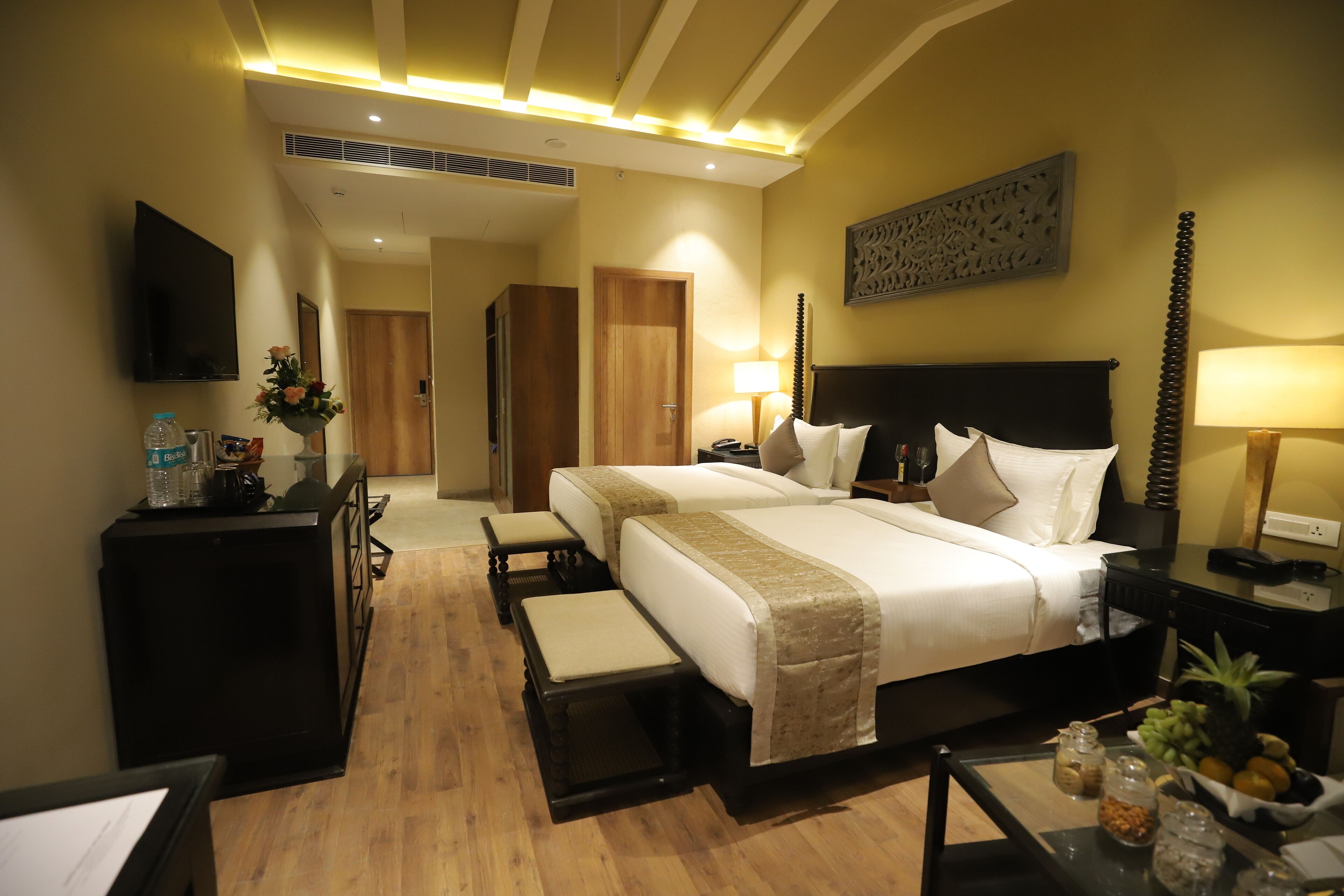 A hotel room with a large bed, bedside tables, a desk, a flat-screen TV, and a decorative wall piece.