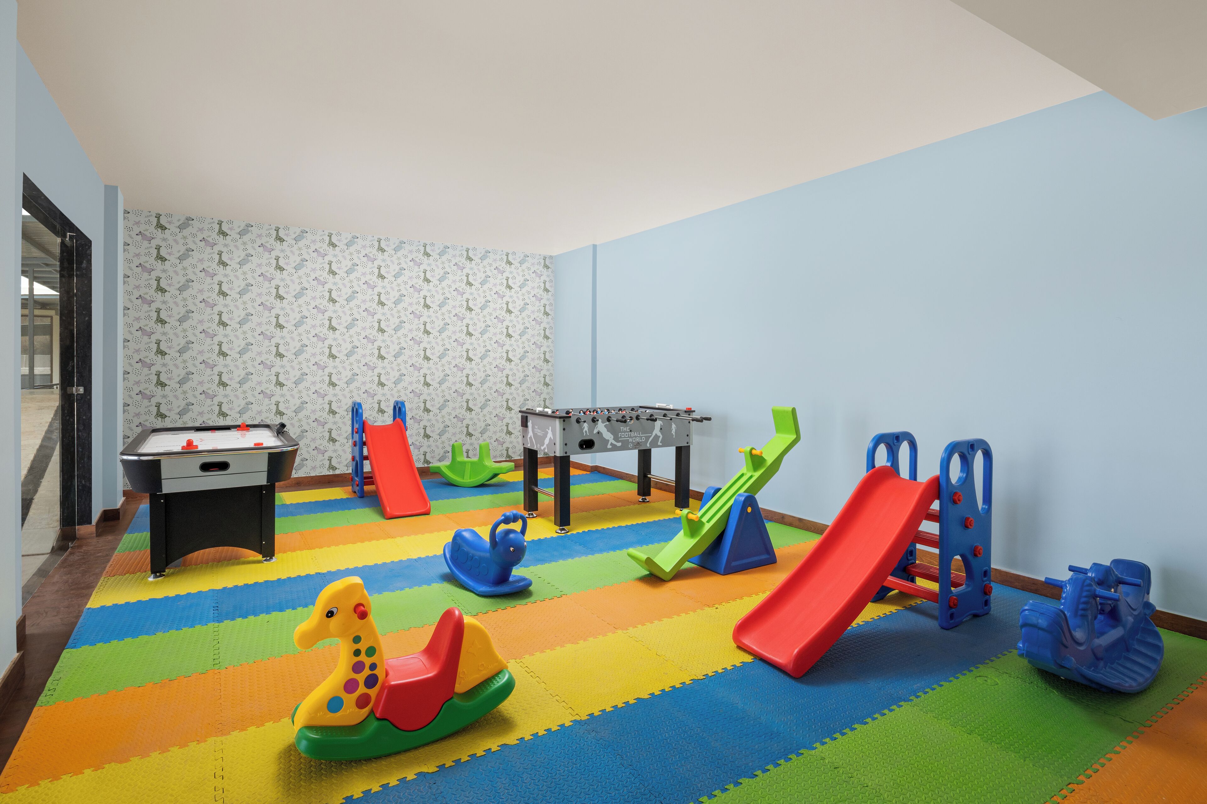 A children's play area with a foosball table, a slide, and various toys on a multicolored foam floor.