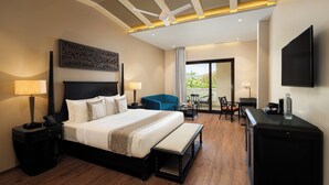 A hotel room with a large bed, a desk with a flat-screen TV, a chair, and a balcony with a table and chairs. - Essentia Udaipur Luxury Resort & Spa (Udaipur)