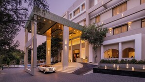 A modern hotel entrance with a covered walkway, a car parked in front, and a water feature. - Essentia Udaipur Luxury Resort & Spa (Udaipur)
