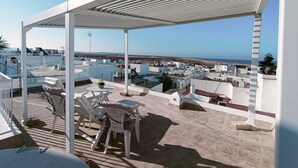 A rooftop terrace with a covered seating area, a view of the sea, and a cityscape in the background. - Casa El Encanto, overlooking the sea. (Conil de la Fra.)