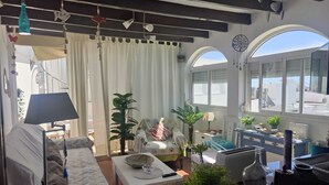A cozy living room with a sofa, a coffee table, and a dining area with a table and chairs. There are potted plants and a decorative item on the windowsill. - Casa El Encanto, overlooking the sea. (Conil de la Fra.)