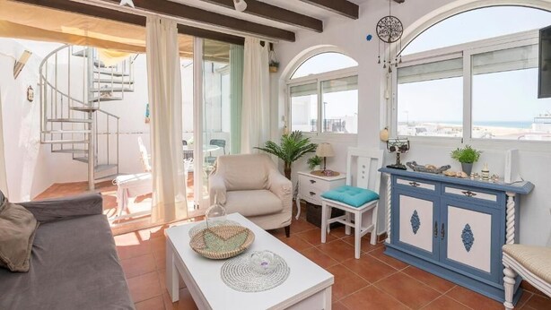 A spacious living area with a sofa, a dining table, and a blue cabinet. There is a spiral staircase leading to an outdoor area. - Casa El Encanto, overlooking the sea. (Conil de la Fra.)