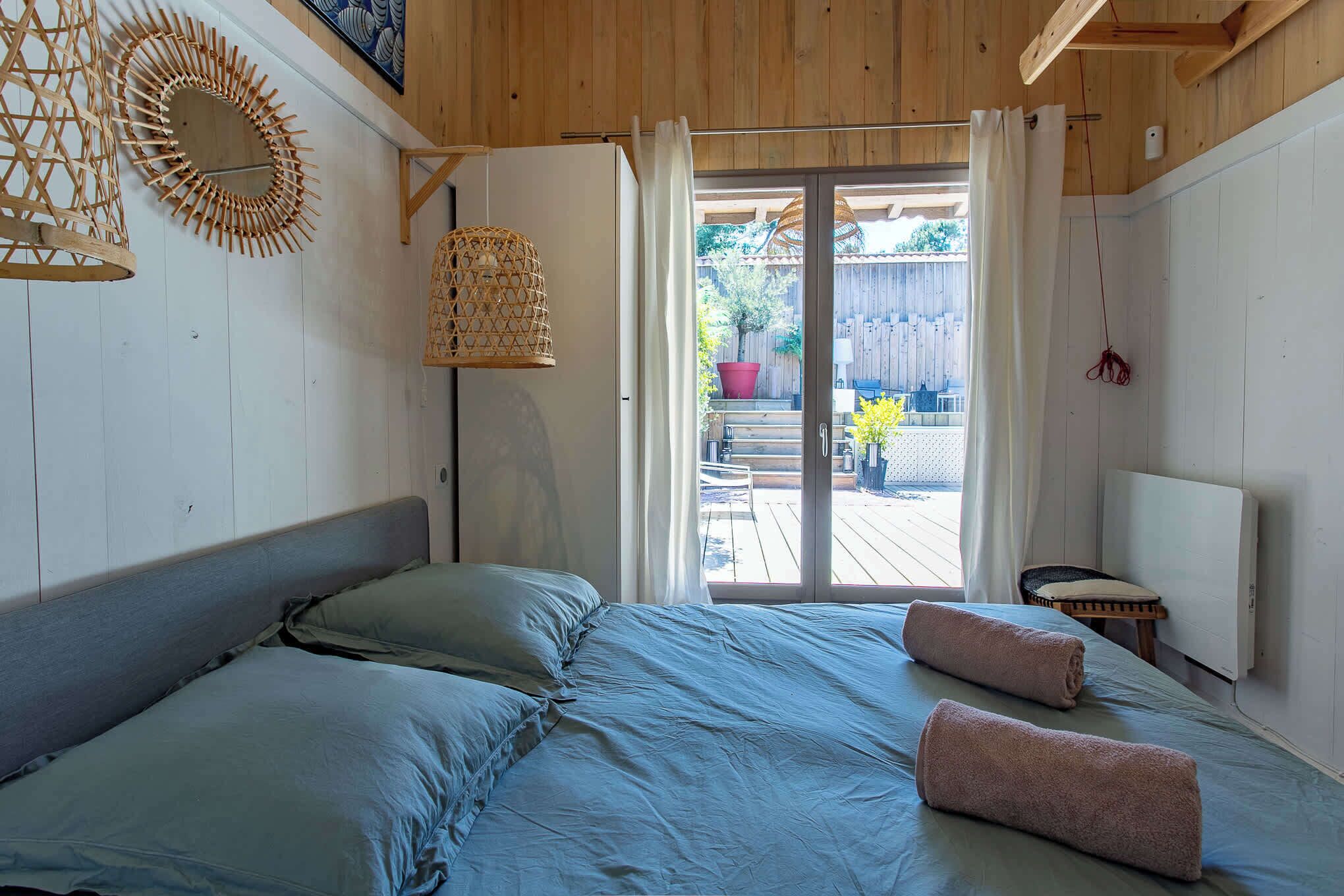 A bedroom with a bed, pillows, a hanging light fixture, a radiator, and a view of the outside.