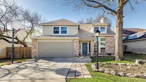 A two-story house with a garage, a front yard with a basketball hoop, and a tree. - 3 King Bedrooms • Hot Tub • Game Room • Near Six Flags & SeaWorld (San Antonio)