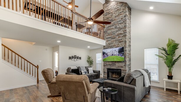 A spacious living area with a stone fireplace, a ceiling fan, and a large TV mounted on the wall. - 3 King Bedrooms • Hot Tub • Game Room • Near Six Flags & SeaWorld (San Antonio)