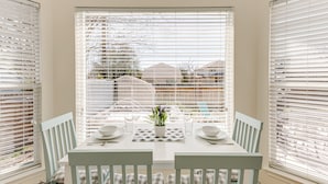 A dining area with a table set for two, white chairs, and a window with blinds. - 3 King Bedrooms • Hot Tub • Game Room • Near Six Flags & SeaWorld (San Antonio)