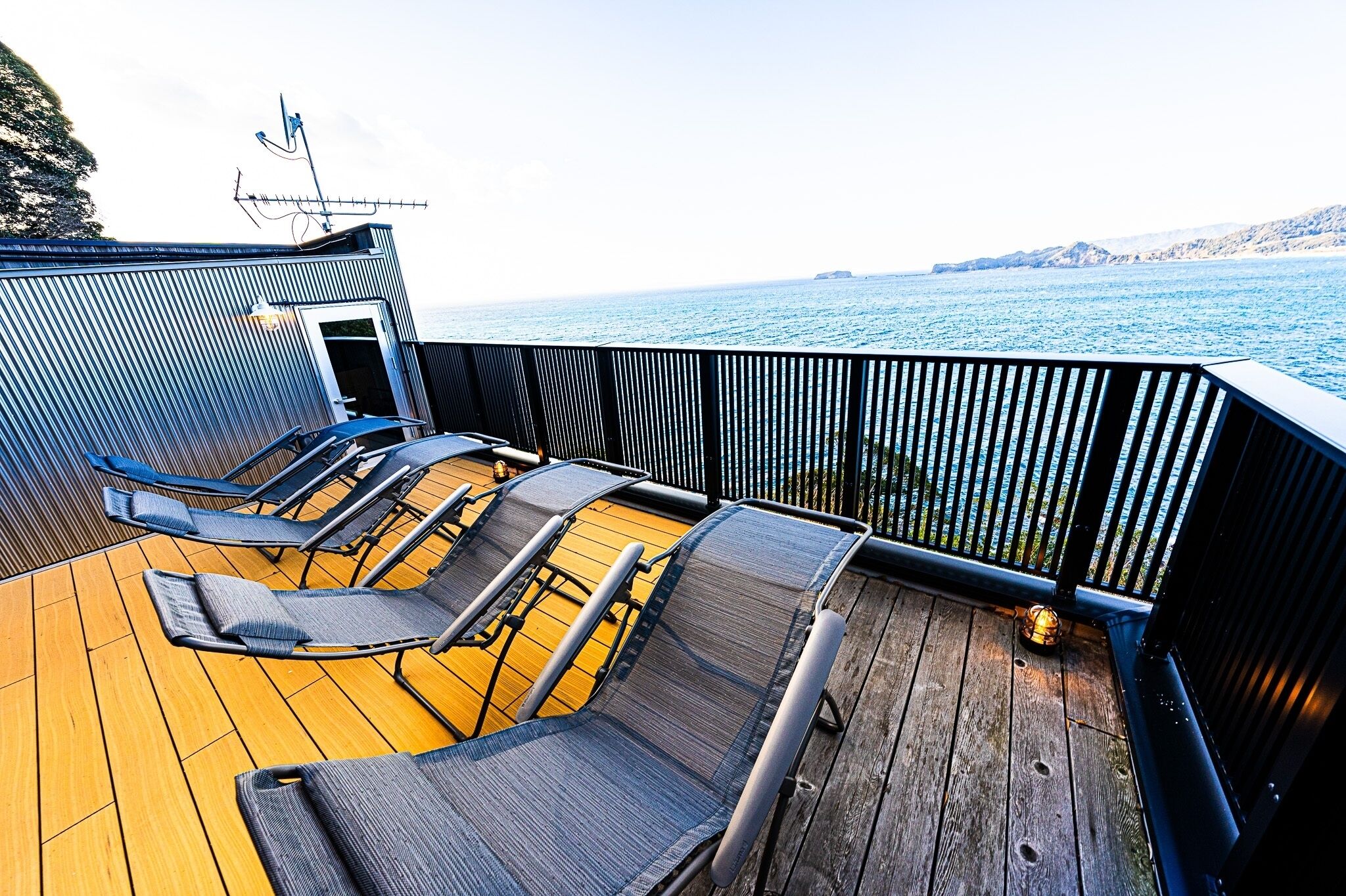 A deck with lounge chairs, a wooden floor, and a view of the sea.