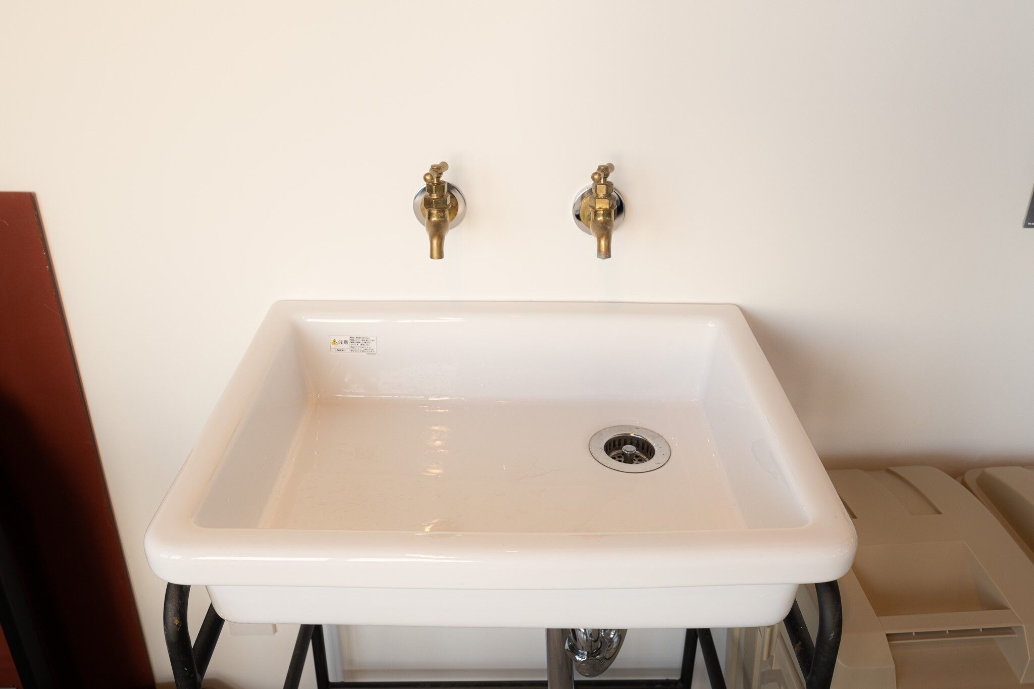 A white rectangular sink with two brass faucets, a drain, and a visible pipe beneath.
