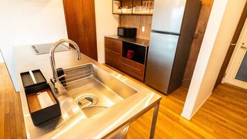 A modern kitchen with a stainless steel sink, wooden cabinets, a microwave, and a refrigerator.