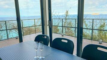 Mesa com duas taças de champanhe numa varanda com vista para a água e terra ao longe.