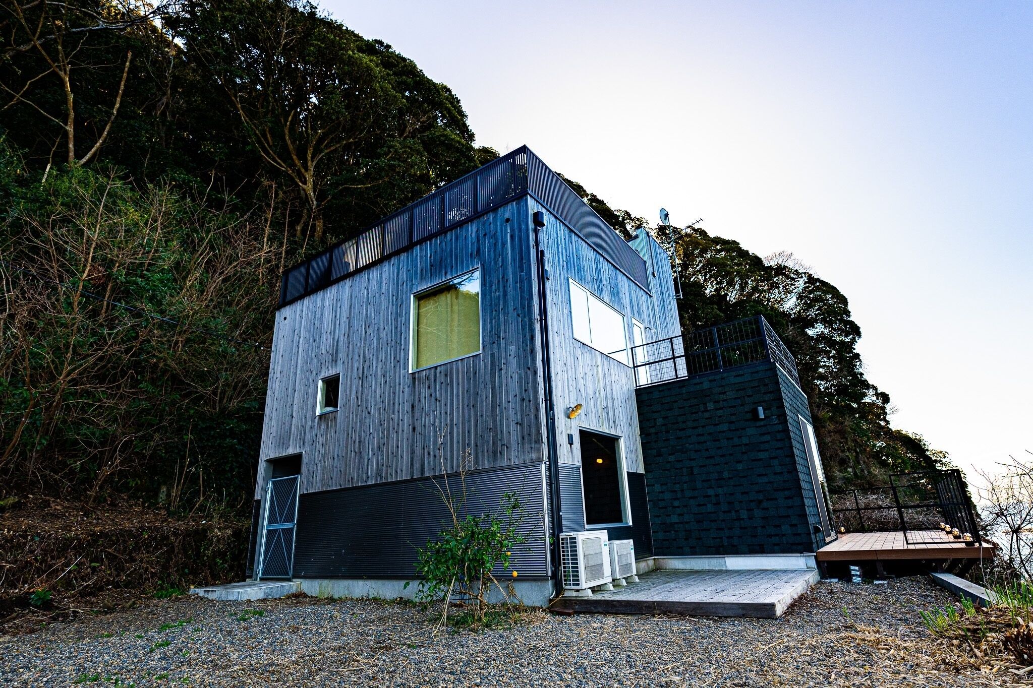 A modern two-story building with a wooden exterior, a large window on the upper floor, and a small deck area.
