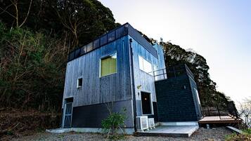 A modern two-story building with a wooden exterior, a large window on the upper floor, and a small deck area.