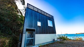 A modern, dark wooden cabin with a metal door and windows, situated by a body of water. - The View minamiboso (Minamiboso)