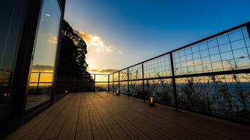 A wooden deck with a glass railing overlooking a body of water and a sunset.