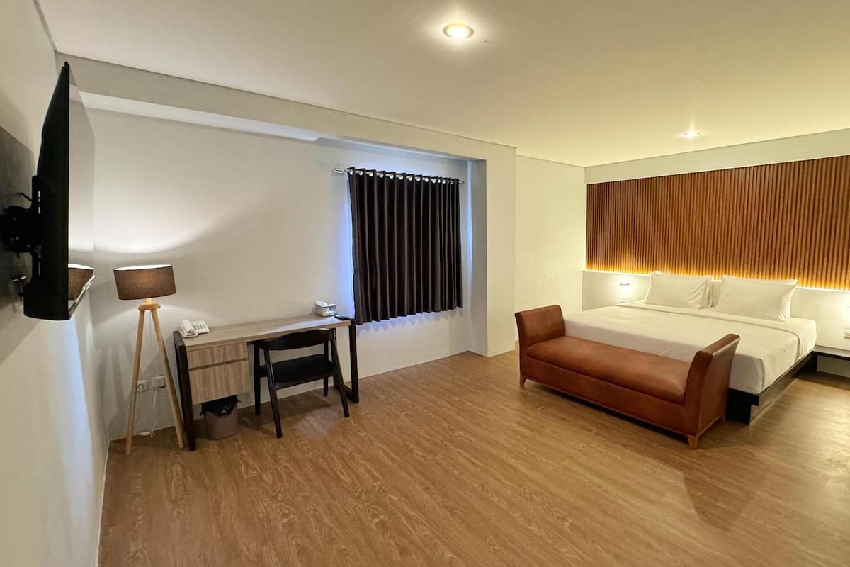 A hotel room with a bed, a desk, a chair, a TV, and a window with curtains.